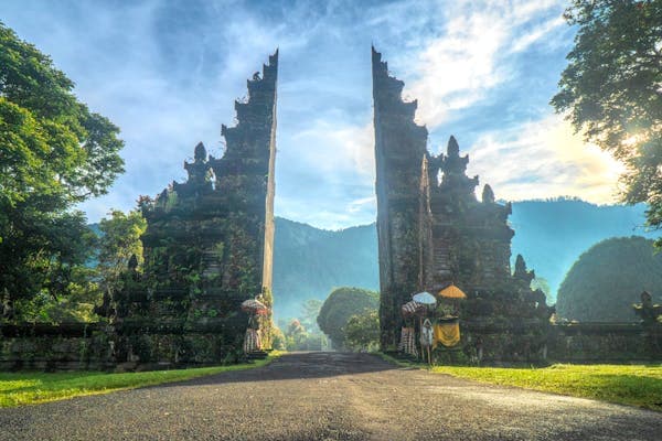 A carved split stone gateway framing a road that runs into forested hills at sunrise