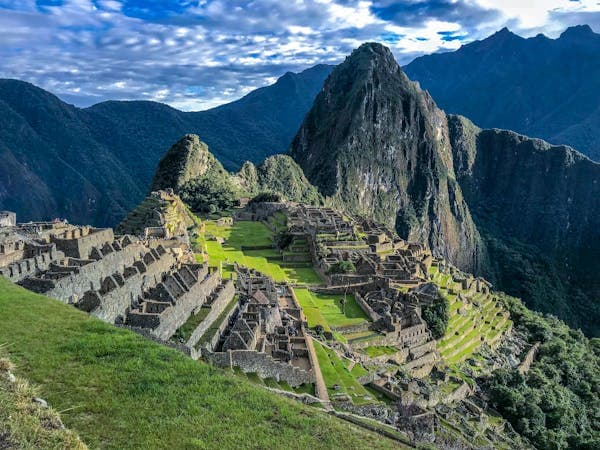Terraced stone ruins on a green mountain ridge with a steep peak rising behind