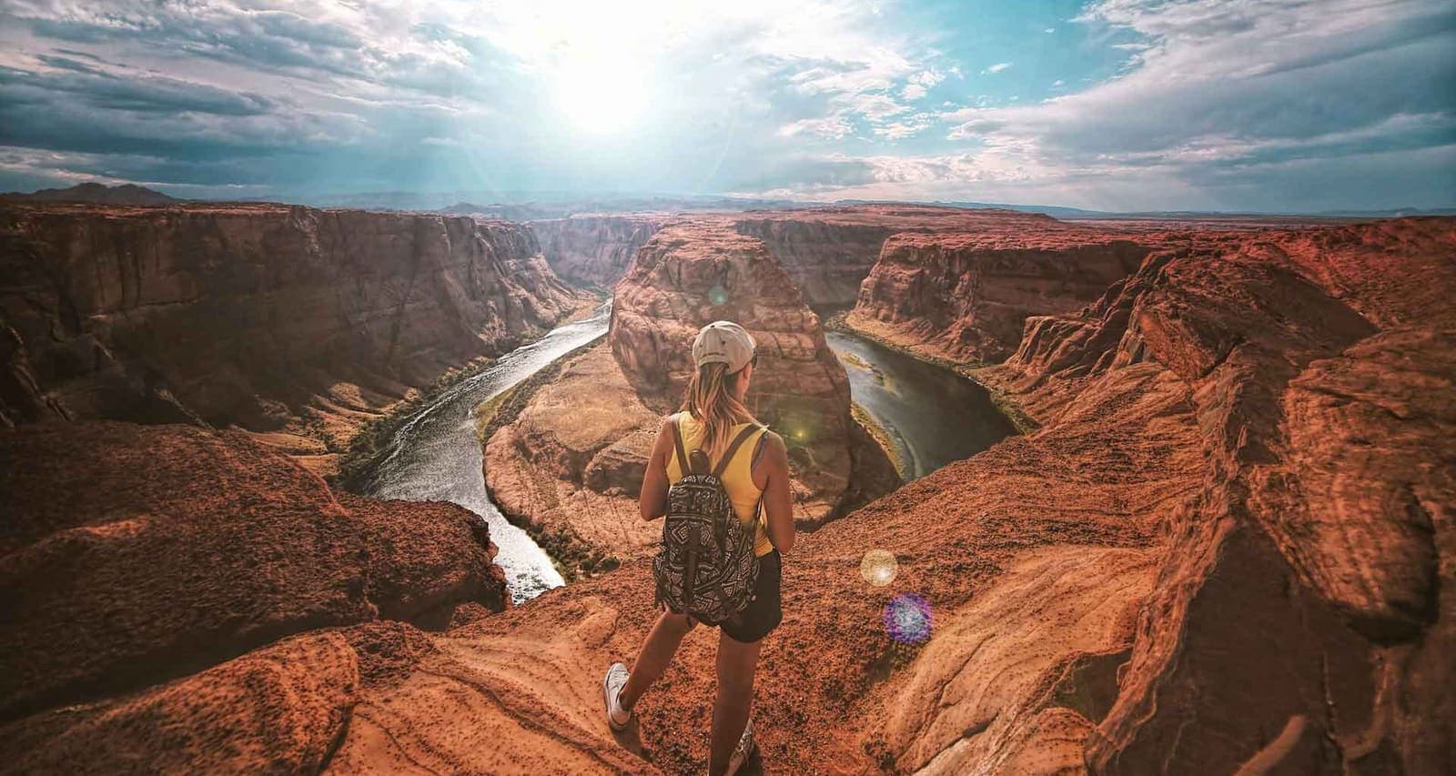 A hiker with a backpack standing on red sandstone above the Colorado River as it loops around Horseshoe Bend